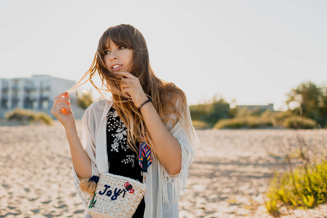 Woman with long hair on beach holding her hair, wearing casual outfit, enjoying sunny day, featured in DIY: Sea Salt Spray article.
