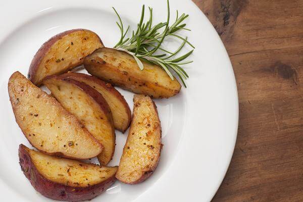 Sweet & Smokey Potato Wedges arranged on a white plate with fresh herbs garnish.