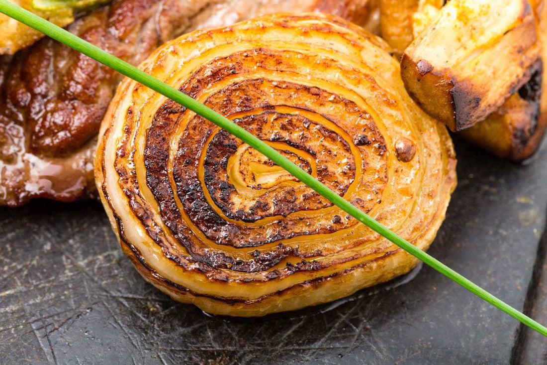 Grilled onion slice with caramelized layers, paired with roasted vegetables on a dark surface.