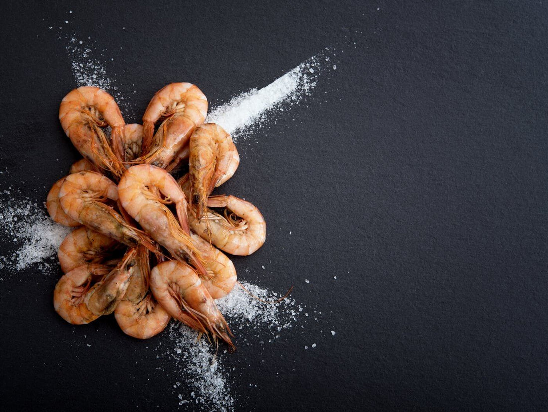 Shrimp de Jonghe Recipe with arranged cooked shrimp on a dark background sprinkled with sea salt.