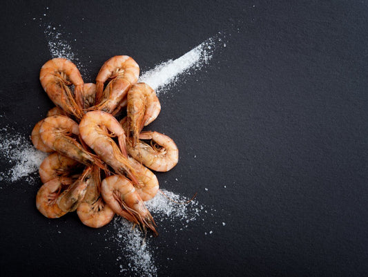 Shrimp de Jonghe Recipe with arranged cooked shrimp on a dark background sprinkled with sea salt.