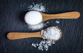 Microplastics in Salt? Fact or Fiction? Sea salt and kosher salt in wooden spoons on a dark surface.